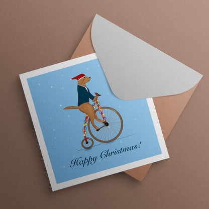 Labrador riding Unicycle wearing Santa hat with Robin sat on handle bars. Christmas Card illustrated by Oundle artist Kitty's Art